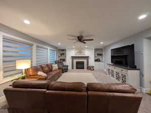 Living area with a glass covered fireplace, built in shelves, a ceiling fan, recessed lighting, and light colored carpet