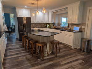 Kitchen with white cabinetry, stainless steel refrigerator with ice dispenser, a kitchen bar, hanging light fixtures, and white dishwasher