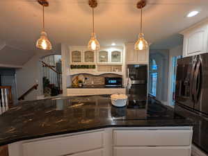 Kitchen with arched walkways, glass insert cabinets, black appliances, dark stone counters, and tasteful backsplash