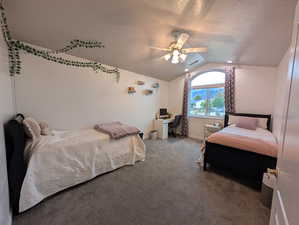 Carpeted bedroom featuring an office area, vaulted ceiling, a textured ceiling, and a ceiling fan