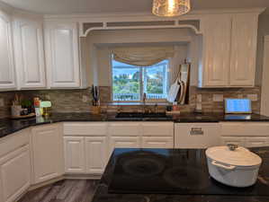 Kitchen with white cabinetry, dark stone counters, tasteful backsplash, dishwasher, and black electric cooktop