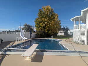 View of swimming pool featuring a patio, a water slide, a fenced backyard, and a diving board
