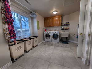 Washroom with light tile patterned floors, cabinet space, and washing machine and clothes dryer
