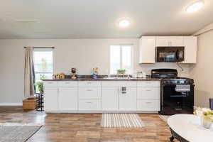 Kitchen with white cabinets, a textured ceiling, black appliances, light wood-style floors, and dark stone countertops