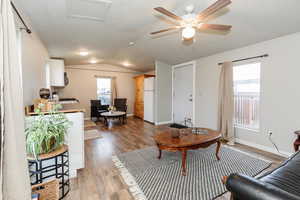 Living room featuring a textured ceiling, dark wood-type flooring, healthy amount of natural light, ceiling fan, and lofted ceiling