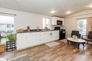 Kitchen featuring black appliances, white cabinets, lofted ceiling, light wood-type flooring, and a textured ceiling