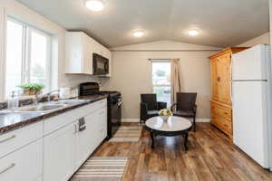 Kitchen featuring black appliances, a textured ceiling, dark wood finished floors, dark countertops, and lofted ceiling