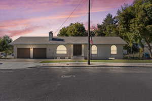 Single story home featuring concrete driveway, brick siding, an attached garage, covered porch, and a chimney