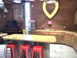 Kitchen featuring brick wall, a kitchen bar, light countertops, a center island, and brown cabinets