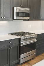 Kitchen with appliances with stainless steel finishes, backsplash, light wood-type flooring, and light stone counters