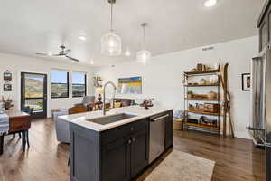 Kitchen with an island with sink, pendant lighting, open floor plan, dark wood-style floors, and stainless steel appliances