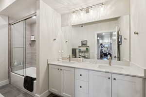 Bathroom featuring double vanity, enclosed tub / shower combo, and dark tile patterned floors