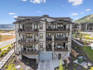 Rear view of property featuring a mountain view, concrete driveway, a balcony, and stone siding