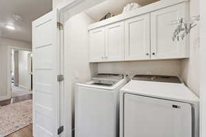 Laundry area with wood finished floors, washer and clothes dryer, and cabinet space