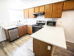 Kitchen featuring brown cabinetry, a peninsula, appliances with stainless steel finishes, light wood-type flooring, and under cabinet range hood