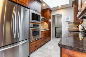 Kitchen featuring appliances with stainless steel finishes, tasteful backsplash, dark stone counters, recessed lighting, and ventilation hood