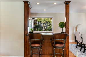Indoor bar featuring light wood-style floors, recessed lighting, ornate columns, and dark stone countertops