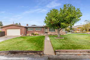 View of front of property featuring brick siding, a front lawn, driveway, and a garage