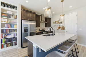 Kitchen featuring dark brown cabinets, stainless steel appliances, backsplash, a breakfast bar area, and an island with sink