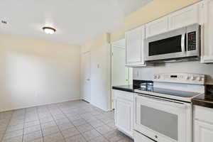 Kitchen featuring white range with electric stovetop, stainless steel microwave, white cabinets, and light tile patterned floors