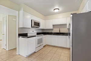 Kitchen with appliances with stainless steel finishes, white cabinetry, light tile patterned floors, and tile counters