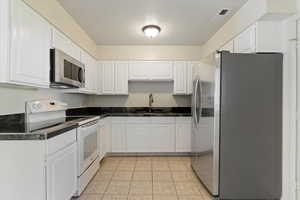 Kitchen featuring dark countertops, appliances with stainless steel finishes, white cabinets, and light tile patterned floors