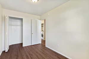 Unfurnished bedroom with dark wood-style flooring, a closet, and washer / clothes dryer