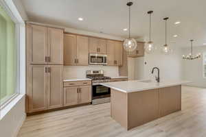 Kitchen with stainless steel appliances, decorative light fixtures, a center island with sink, light brown cabinetry, and recessed lighting