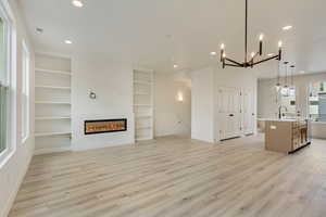 Kitchen featuring decorative light fixtures, built in shelves, an island with sink, open floor plan, and a glass covered fireplace