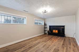 Unfurnished living room with wood-type flooring, a textured ceiling, and a wood stove