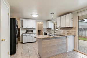 Kitchen featuring white cabinets, a peninsula, black appliances, light tile patterned floors, and light stone counters