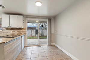 Kitchen with light tile patterned flooring, light stone countertops, white cabinetry, backsplash, and black electric stovetop
