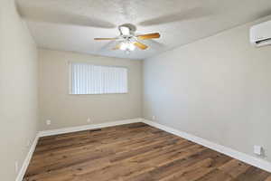 Unfurnished room with a textured ceiling, dark wood-type flooring, a wall mounted AC, and a ceiling fan