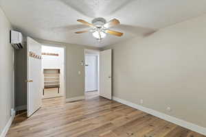 Unfurnished bedroom with a textured ceiling, a spacious closet, a ceiling fan, light wood-style floors, and a wall unit AC