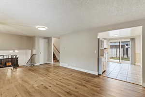Unfurnished living room with a textured ceiling, light wood-style flooring, and stairway