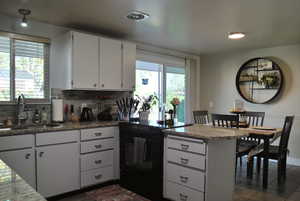 Kitchen featuring a peninsula, black range with electric stovetop, light stone counters, white cabinets, and tasteful backsplash