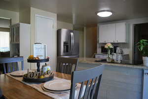 Kitchen with light stone counters, white cabinetry, stainless steel refrigerator with ice dispenser, and black electric stovetop
