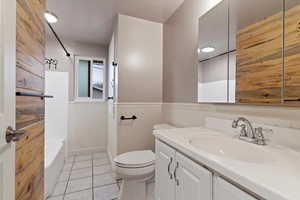 Bathroom with wainscoting, vanity, light tile patterned floors, and shower / washtub combination