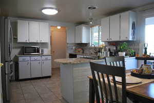Kitchen with white cabinets, stainless steel appliances, tasteful backsplash, light tile patterned floors, and light stone countertops