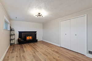 Unfurnished living room with a textured ceiling, a warm lit fireplace, light wood-style flooring, and ornamental molding