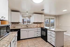 Kitchen featuring a peninsula, black appliances, tasteful backsplash, light stone counters, and white cabinetry