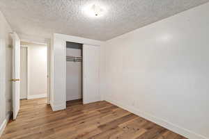 Unfurnished bedroom with a textured ceiling, a closet, and wood finished floors
