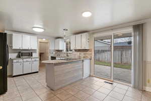 Kitchen with white cabinets, a peninsula, black appliances, light stone countertops, and decorative backsplash