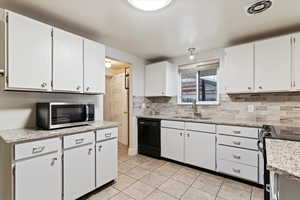Kitchen featuring appliances with stainless steel finishes, white cabinetry, and light stone counters