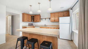 Kitchen featuring freestanding refrigerator, a kitchen island, tile countertops, a breakfast bar, and light colored carpet