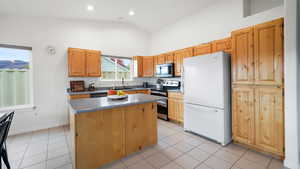 Kitchen with stainless steel appliances, a kitchen island, light tile patterned floors, vaulted ceiling, and dark countertops