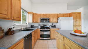 Kitchen featuring appliances with stainless steel finishes, light tile patterned flooring, dark countertops, and light brown cabinets