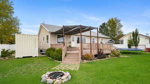 Rear view of house with a fenced backyard, a fire pit, a trampoline, and a wooden deck