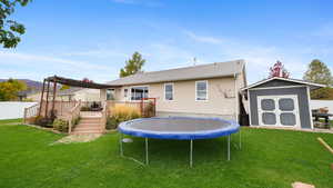 Back of house with a shed, a wooden deck, and a trampoline