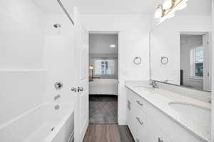 Full bathroom with double vanity, washtub / shower combination, ensuite bathroom, and dark wood-style flooring